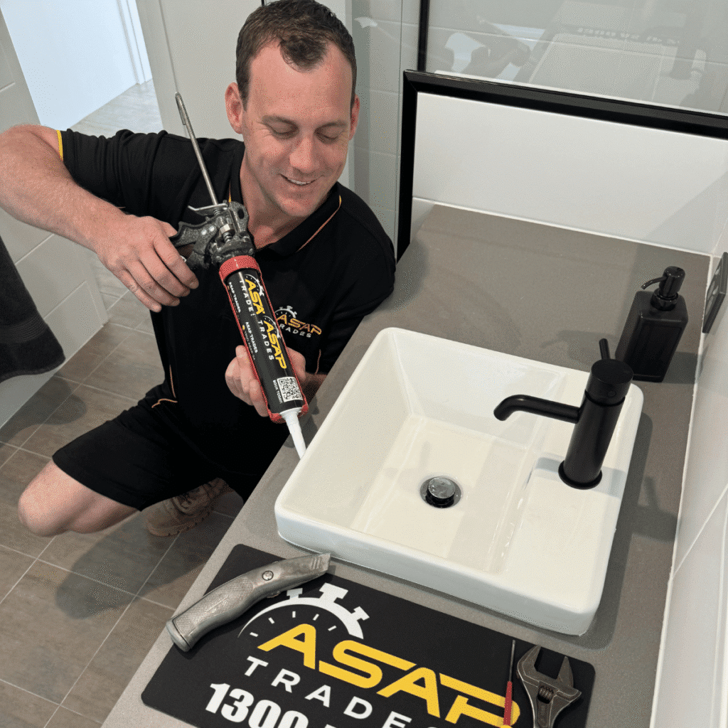 One of the owners at asap trades finishing up a kitchen sink with a caulking gun in perth
